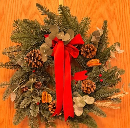 Reviewer's finished Christmas wreath from the workshop, with a red ribbon, pine cones, and dried oranges.