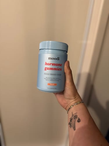 Customer holding a light blue bottle of moodi Peach hormone gummies.