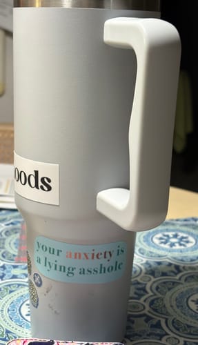 Customer's "Your anxiety is a lying asshole" text sticker applied to a light-colored travel mug.