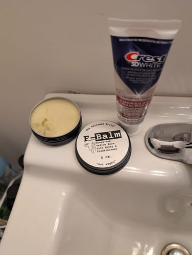 Customer's open tin of F-Balm tallow balm on a bathroom sink next to its lid.