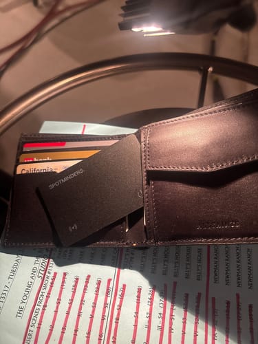 Customer's black SPOTMINDERS Tracking Card partially inserted into an open brown wallet.