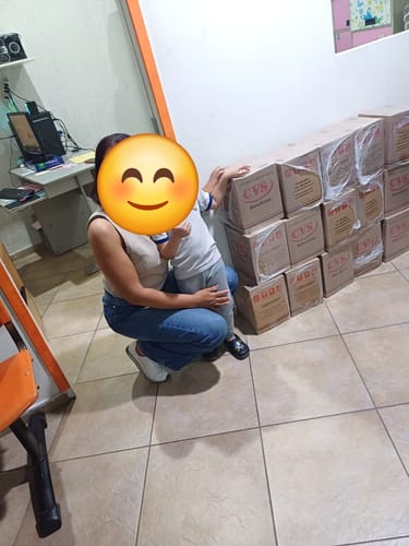 Cliente com uma criança ao lado de várias caixas empilhadas da Cesta Básica Econômica Júnior.