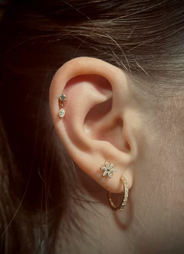 Kundin zeigt das getragene, blumenförmige Blossom Piercing am Ohr, zusammen mit anderen Ohrringen.