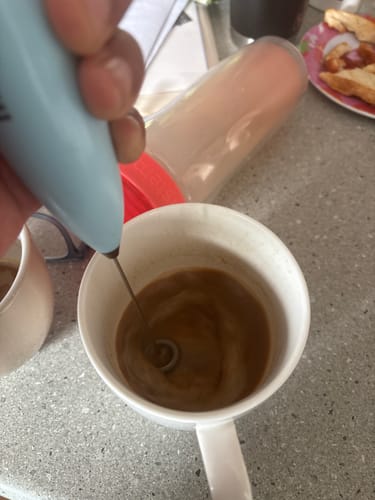 Close-up of a reviewer using the blue Electric Mixer to froth a drink in a white mug.