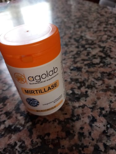 Recensore mostra il flacone del prodotto Mirtillase con tappo arancione su un bancone di marmo.