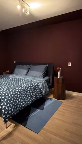 Klant toont de bordeauxrode HAY Facet bijzettafel als nachtkastje in een slaapkamer.