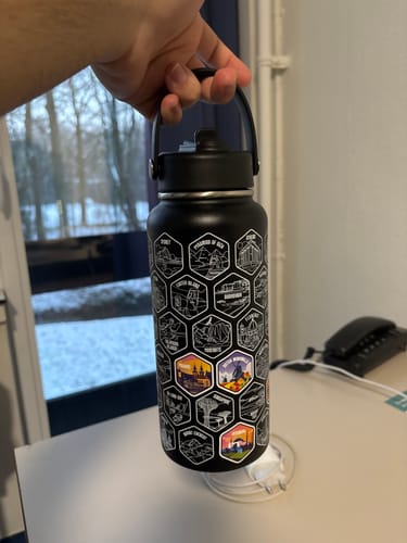 Customer holding the black World Explorer Bottle, showing several colorful stickers on its destination grid.