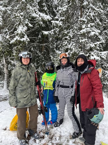 Customer wearing the patterned one-piece ski suit with a faux fur hood, posing with a group in a snowy setting.