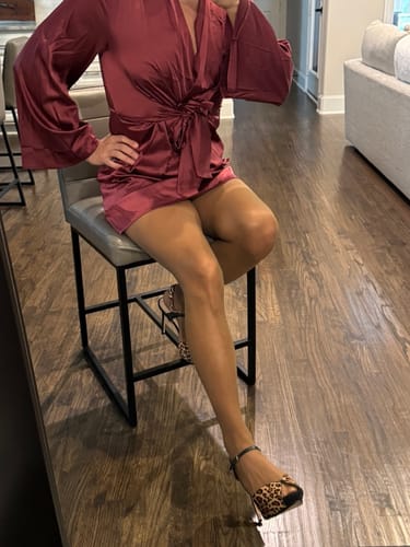 Customer sitting on a stool, wearing the glossy PLAY Free Hugging Seamless Tights with a dress and heels.