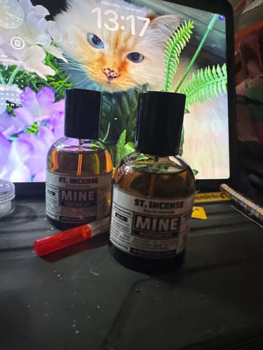 Recensore mostra la boccetta di profumo ST. INCENSE su una scrivania, vicino a una seconda boccetta.