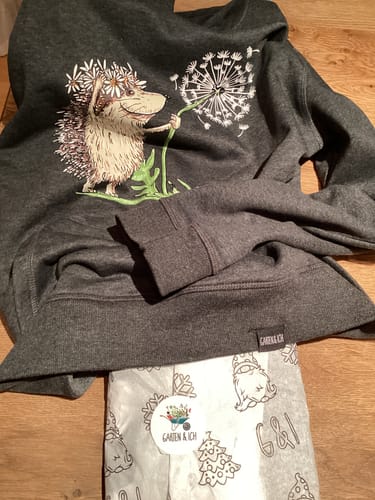 Kunde zeigt ein graues Sweatshirt mit einem Igel-Aufdruck, das auf dem dazugehörigen Verpackungspapier liegt.