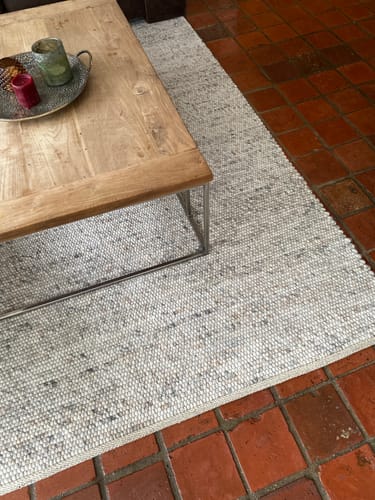 Klant toont het gemêleerde by fonQ Dots vloerkleed op een tegelvloer onder een houten salontafel.