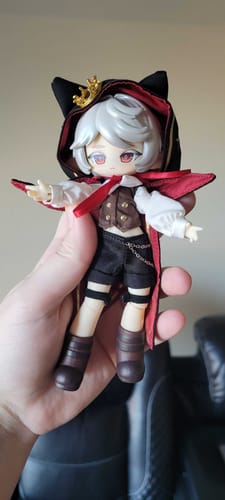 Customer holding the Astra BJD action figure. It has white hair and wears a detailed black and red hooded cape with cat ears.