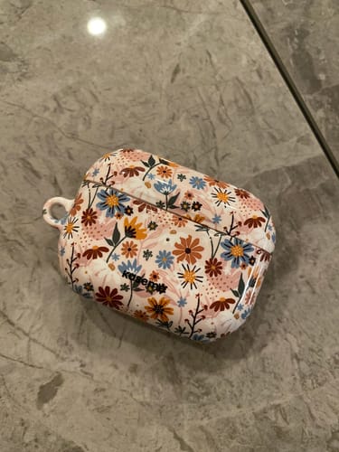 Customer's Emily AirPods Case with a vibrant floral pattern, seen on a gray marble surface.