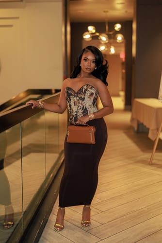 Customer wearing the dark, body-contouring NW Midi Skirt with a corset top in a hallway.
