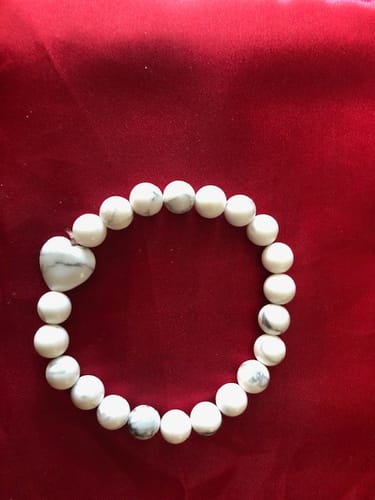 Reviewer's white Howlite bracelet with a single heart-shaped bead on a red surface.