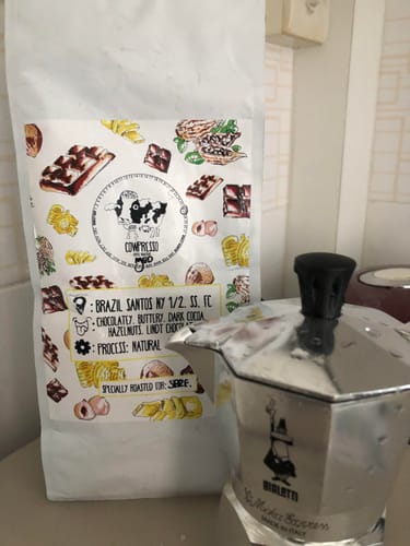 Customer's bag of Brazil Santos coffee, showing the old packaging, placed next to a silver moka pot.
