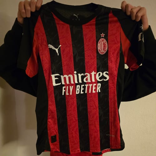 Un cliente mostra la Maglia Milan Home 2025/26 a strisce rosse e nere.