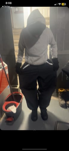 Customer wearing the very baggy black snow pants with a grey hoodie indoors.
