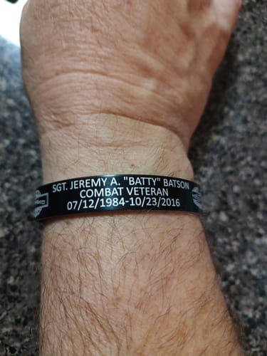 Customer's wrist wearing a black bracelet with custom engraving for a combat veteran.