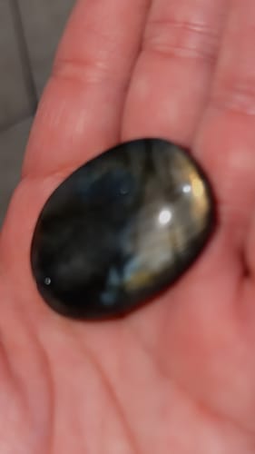 Close-up of a reviewer holding a dark, polished Labradorite crystal in their palm.
