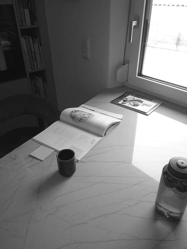 Kundenfoto, aufgenommen mit der NUVINT Digitalkamera: eine stimmungsvolle Schwarz-Weiß-Aufnahme eines Tisches mit Buch und Tasse.