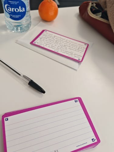 Un client montre ses fiches FLASH 2.0 OXFORD lignées sur un bureau, avec une pile neuve et une fiche manuscrite.