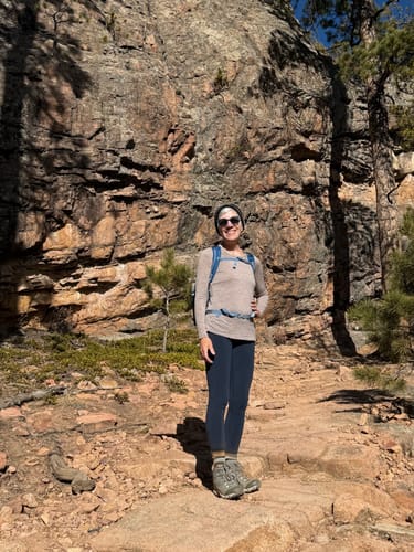 Reviewer smiling on a rocky trail while wearing the dark Piper Pocket Leggings.