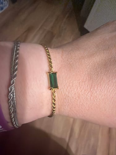 Customer's wrist wearing the gold Castellanos Bracelet with a rectangular green stone, layered with a silver bracelet.