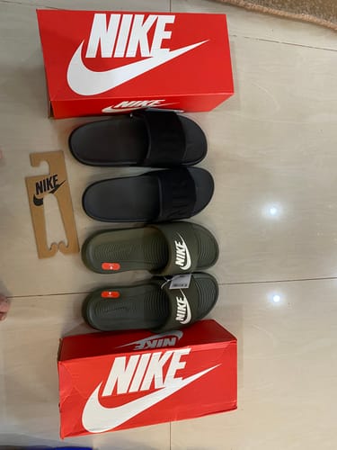 Customer's two pairs of Nike Victori One Slides, one black and one olive green, displayed on the floor with their red Nike boxes.
