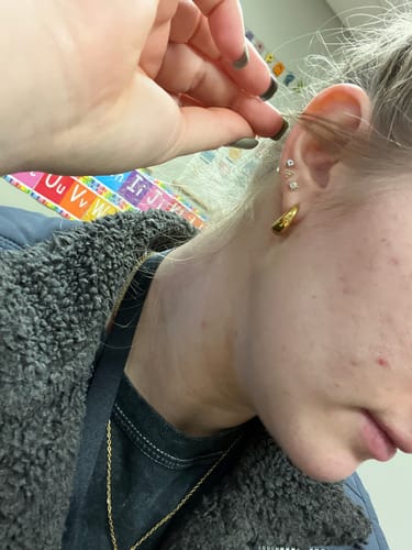 Close-up of a reviewer's ear showing a single gold Mini Drop Huggie earring.