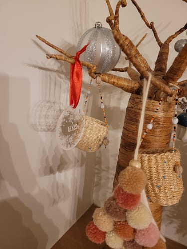 Recensent toont gepersonaliseerde Sneeuwvlokjes Plexiglas Kerstbal met de naam 'Gloria' hangend in een decoratieve boom.