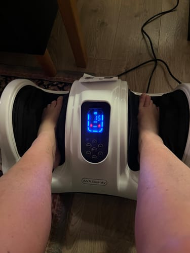 En anmelder bruger fod- og lægmassageapparatet. Det hvide apparats oplyste blå display viser 15 minutter.