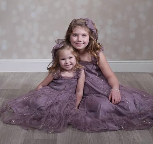 Customer's two children sitting on the floor wearing matching sparkly Glimmer Dresses in Sugared Plum.