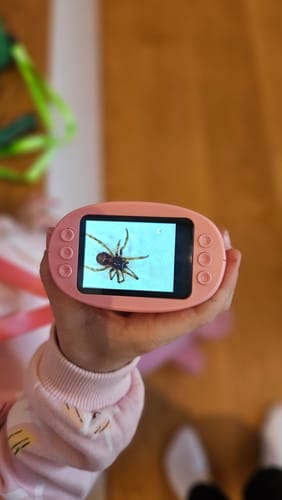 Ein Kunde hält das rosa Abenteuer-Mikroskop in der Hand, auf dessen Bildschirm eine stark vergrößerte Spinne zu sehen ist.