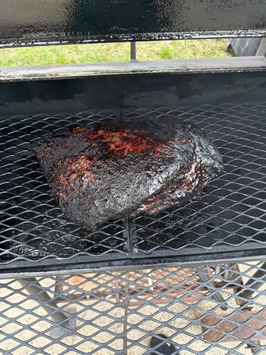 Customer's USDA Prime Brisket with a dark, seasoned crust resting on the grates of a smoker.