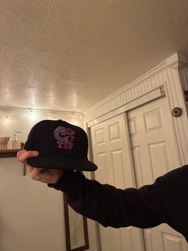 Reviewer holding a custom black baseball cap with a teal and pink 3D puff embroidered logo.