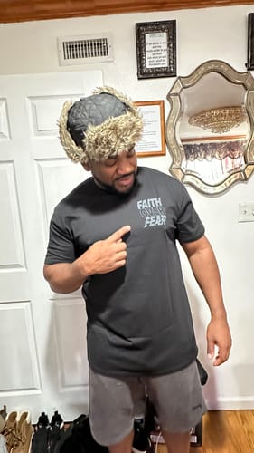 Reviewer pointing to the small 'Faith Over Fear' graphic on the front of their black Mystery Tee.