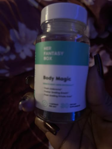 Customer's hand holding a clear bottle of Her Fantasy Box Body Magic pills in dim lighting.