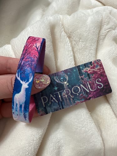 Customer's hand holding the Patronus wristband and matching holographic card from the Winter Wonders Collection.