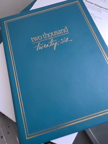 Customer's teal 2026 Essential Planner, showing the gold-embossed text and border on the cover.