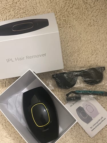 Anmelder viser den sorte IPL-hårfjerner i sin æske med tilbehør som solbriller og en skraber.