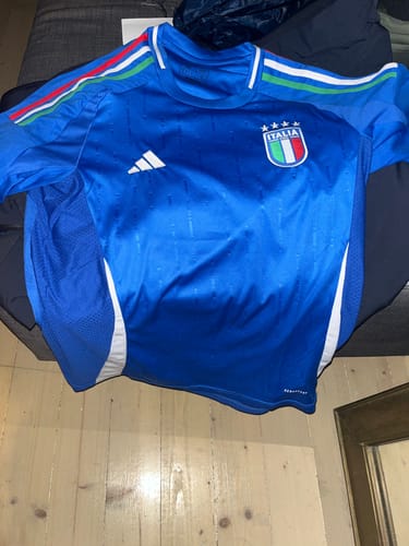 Un cliente mostra la MAGLIA ITALIA HOME 2024/25 blu stesa su una superficie.
