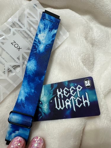 A customer's blue Keep Watch Watch Band with a dragon design, laid out on a soft white surface next to its collector's card.