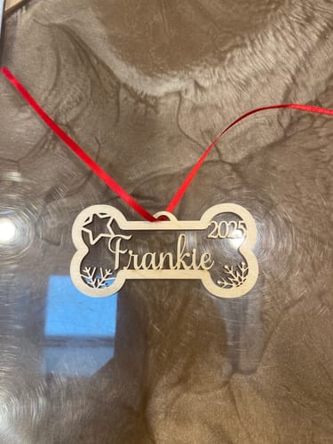 Customer's personalized wooden dog bone ornament, engraved with the name 'Frankie' and the year 2025, with a red ribbon.
