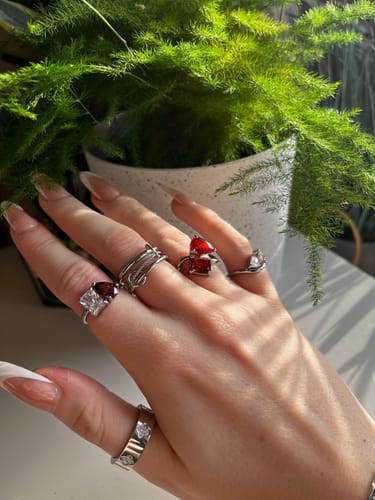 Reviewer's hand showing the Toi Et Moi Birthstone Ring with clear and red stones, styled with other silver-toned rings.