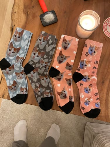 Rezensent zeigt vier Paar bunte, individuelle Socken mit aufgedruckten Katzengesichtern auf einem Holztisch.
