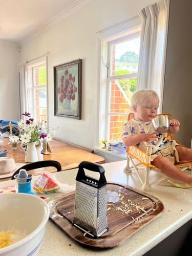 A reviewer's baby sits in the Parker baby chair v2 on a kitchen counter, helping with baking.