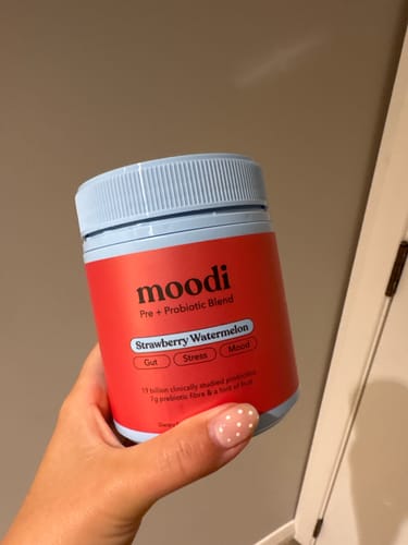 Customer holding a red tub of Moodi Strawberry Watermelon pre and probiotic blend in their hand.