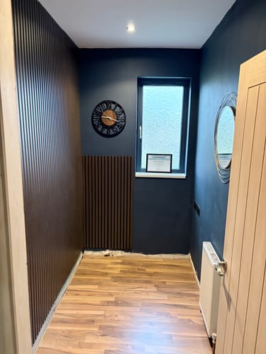 Customer's dark brown acoustic slatted wall panels installed as a feature wall and under a window in a modern hallway.
